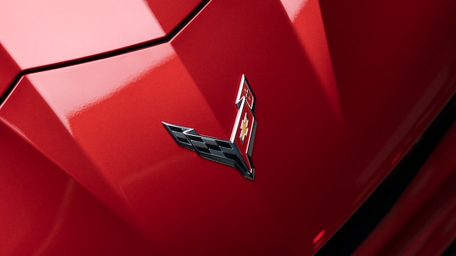 A close-up shot of the Corvette crossed-flags emblem on the front of a red Corvette Z06.