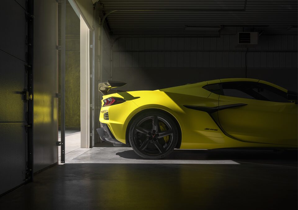 The rear of a yellow Corvette Z06, illuminated by an open garage doorway behind it.