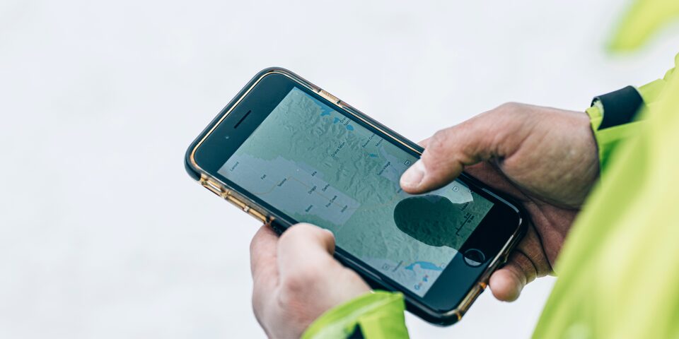Un hombre con una chaqueta verde neón sosteniendo su smartphone y tocando la pantalla.