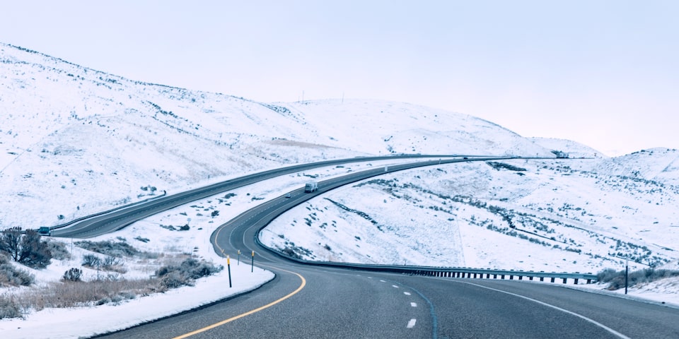 Una carretera de cuatro carriles dividida que serpentea a lo largo de colinas nevadas.