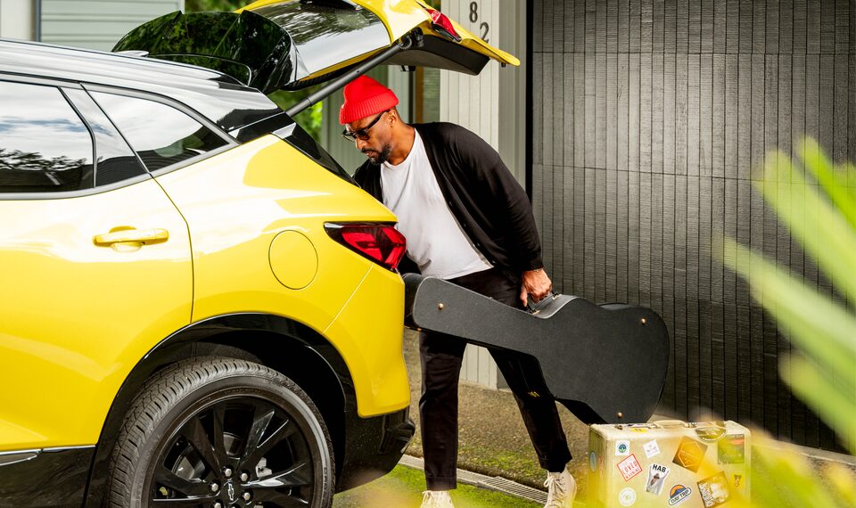 Redray Frazier loads a guitar and other equipment into the back of a bright yellow Blazer.