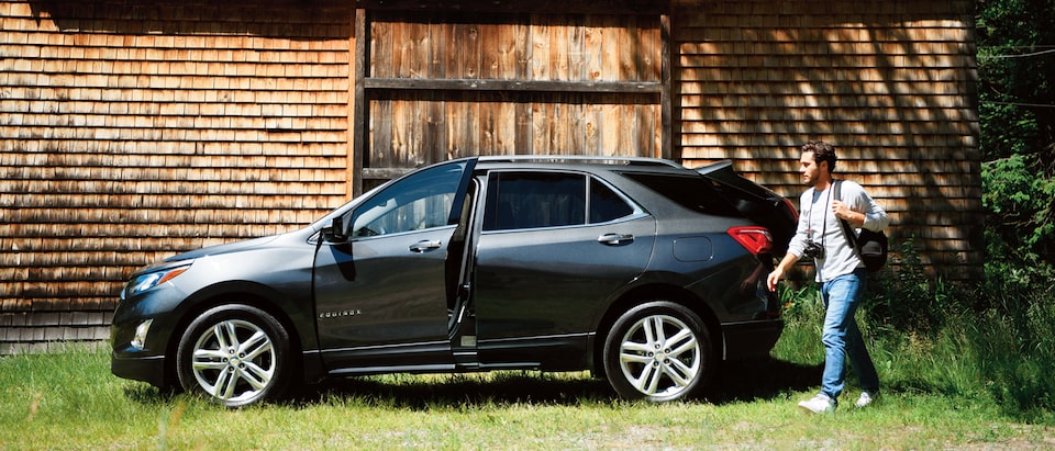 A man with a camera walking past a Chevrolet Equinox in front of an old wood-shingled home.