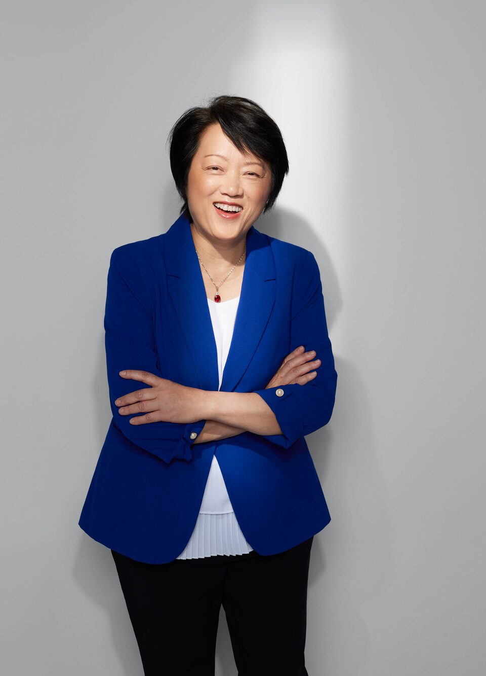 Mei Cai, directora de investigación en sistemas de celdas de baterías de GM, posa de pie con los brazos cruzados y sonriendo a la cámara.