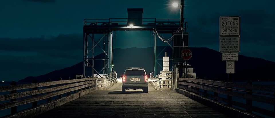 The rear of a Chevy Tahoe SUV as it waits to drive onto a car ferry at night.