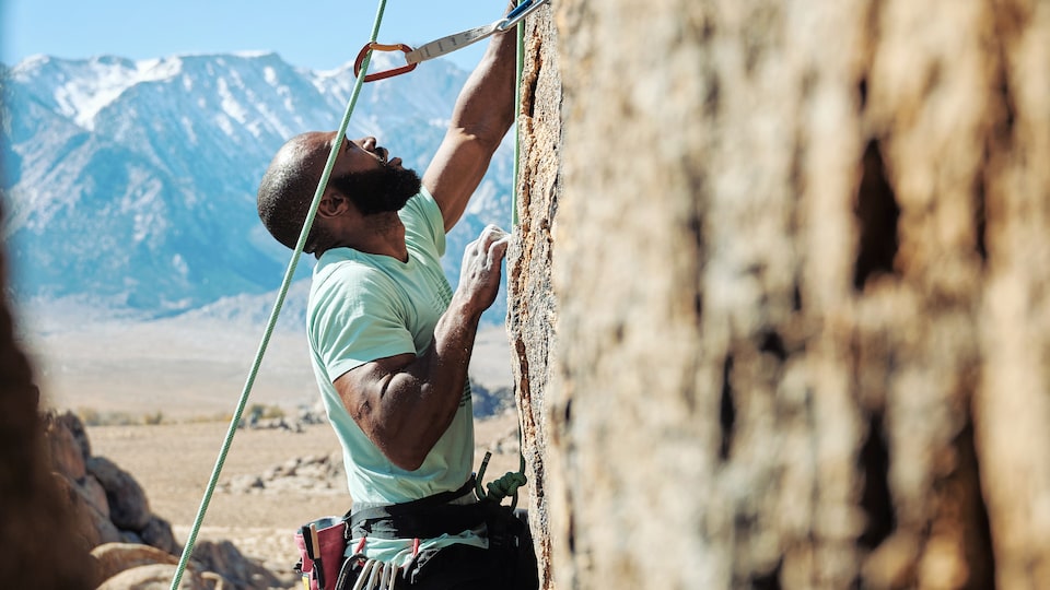Una persona escalando una ladera rocosa escarpada, con cuerdas que se extienden hacia arriba y hacia abajo de ella.