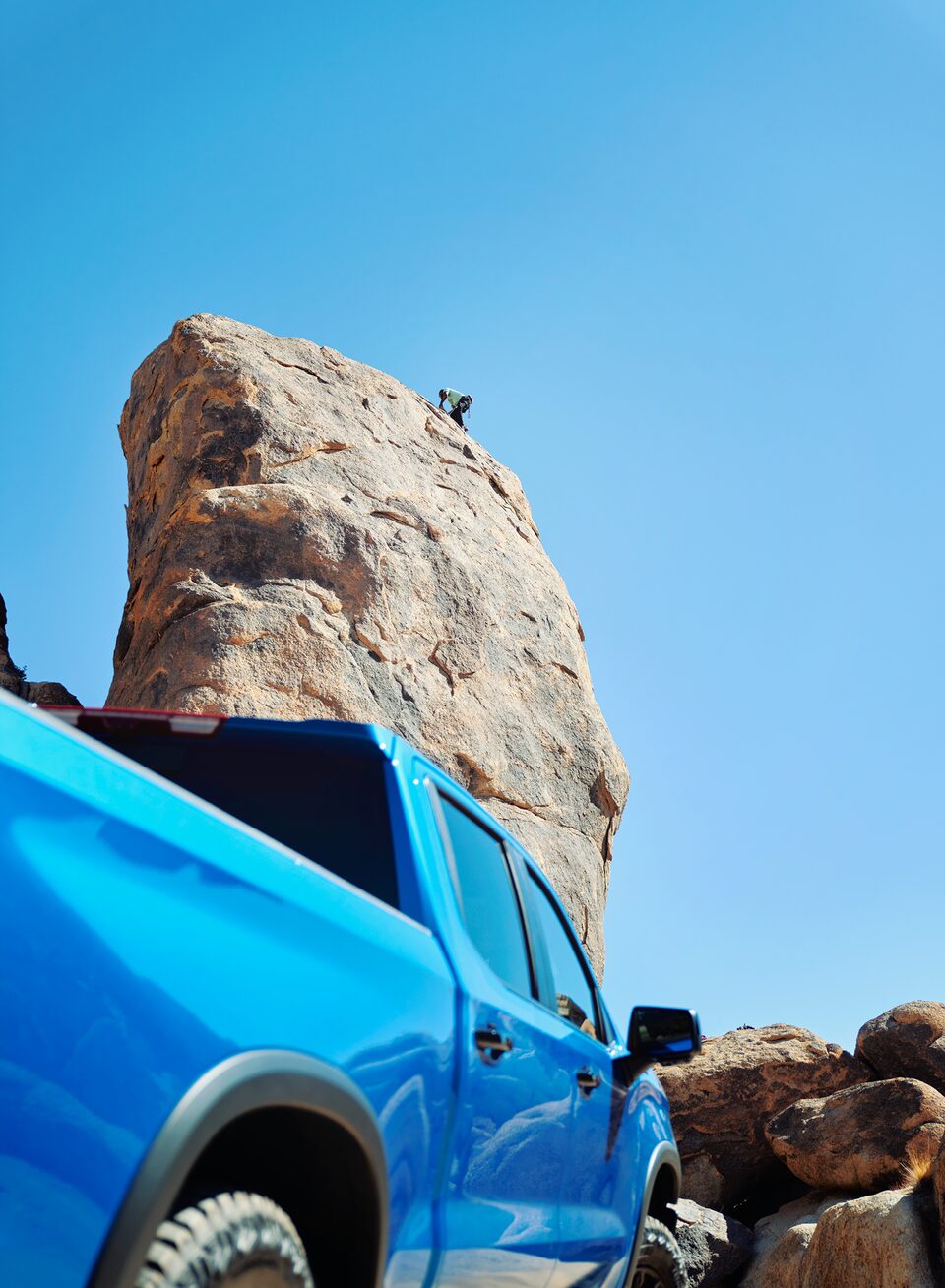 Mirando hacia la parte superior de un enorme bloque de roca con saliente, desde un punto de vista bajo al lado del guardafangos trasero de una Silverado ZR2 azul.