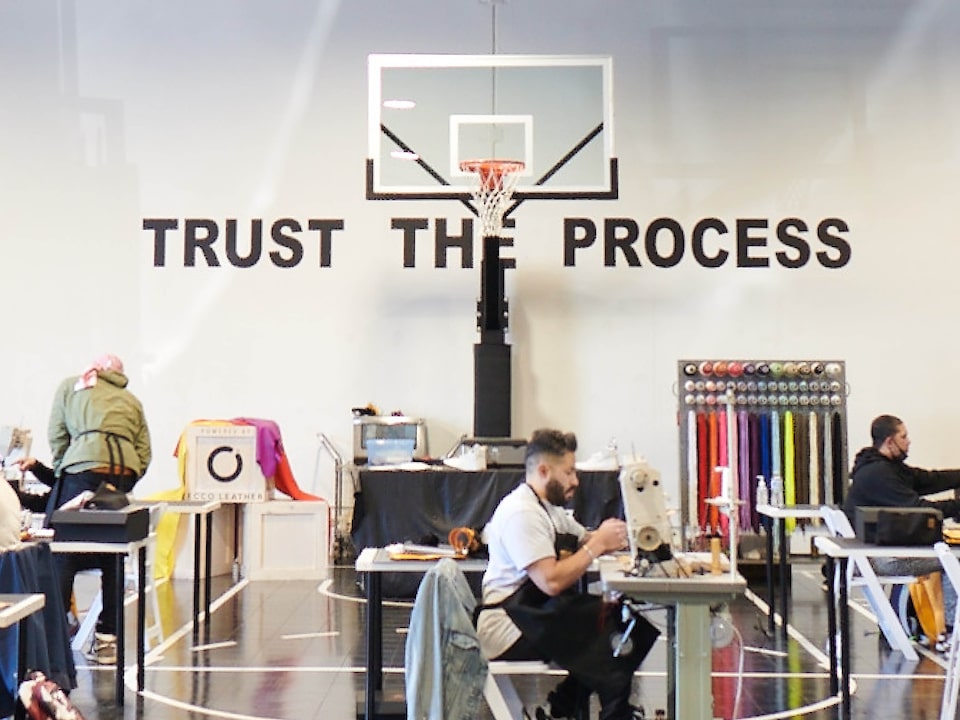 The Sneaker School se instaló en el gimnasio de una escuela, con casi una docena de personas sentadas en mesas con máquinas de coser. Un letrero detrás de una canasta de básquetbol que dice <em>Trust the Process</em> (Confía en el proceso).