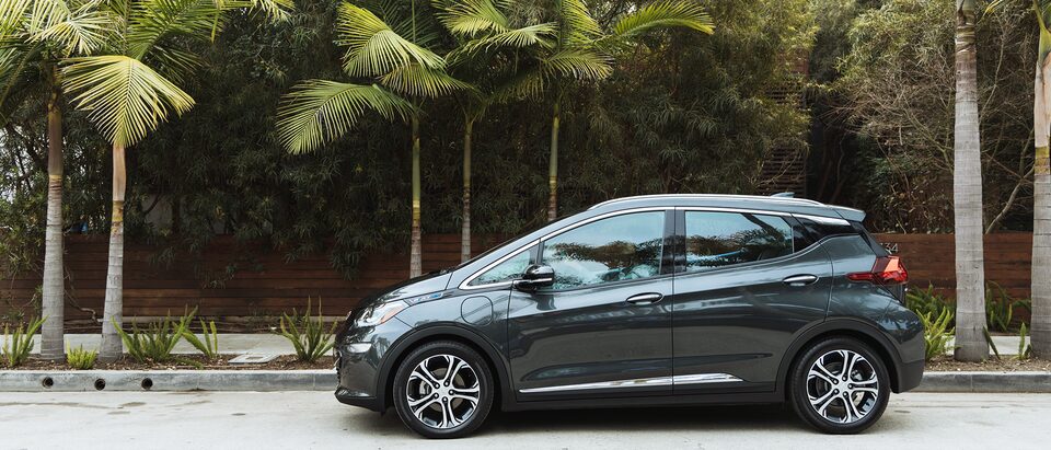 Un Bolt EV color gris oscuro está en una calle con palmeras en el fondo.