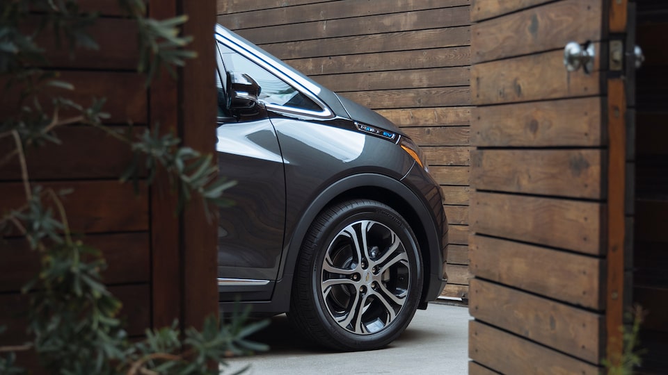 El extremo delantero de un Chevrolet Bolt EV color gris oscuro se ve desde una puerta de madera.