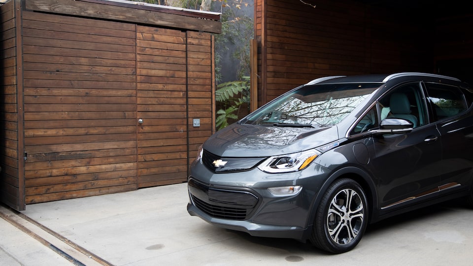 Un Chevrolet Bolt EV color gris oscuro saliendo de un garaje de madera.