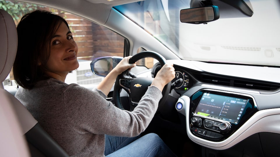 Una mujer está sentada en el asiento del conductor de un Chevrolet Bolt EV y mira hacia atrás, sonriendo.