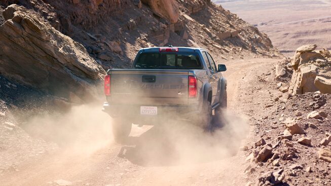 A gray Chevy Colorado ZR2 Bison is seen from behind on a dusty dirt road with red rocks on both sides.
