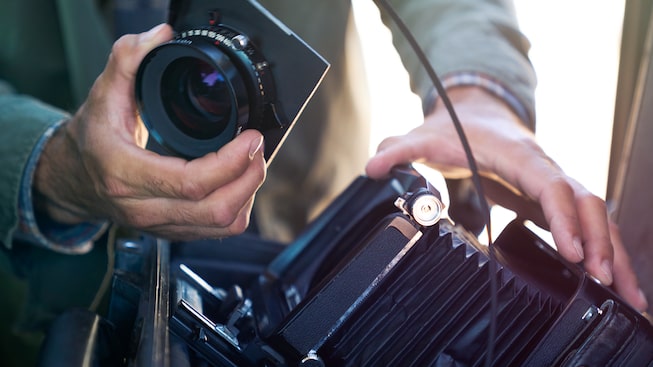 A person's hands assemble a lens onto a large-format camera.