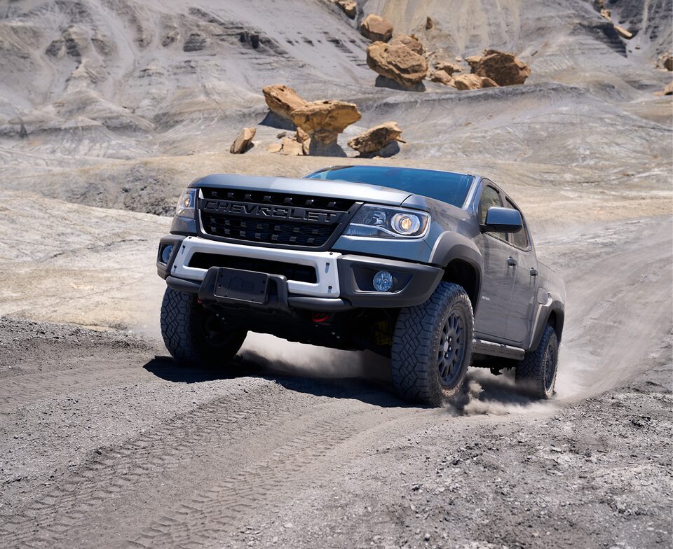A gray Chevy Colorado ZR2 Bison tops a steep hill on a dirt road, with red rocks in the background.