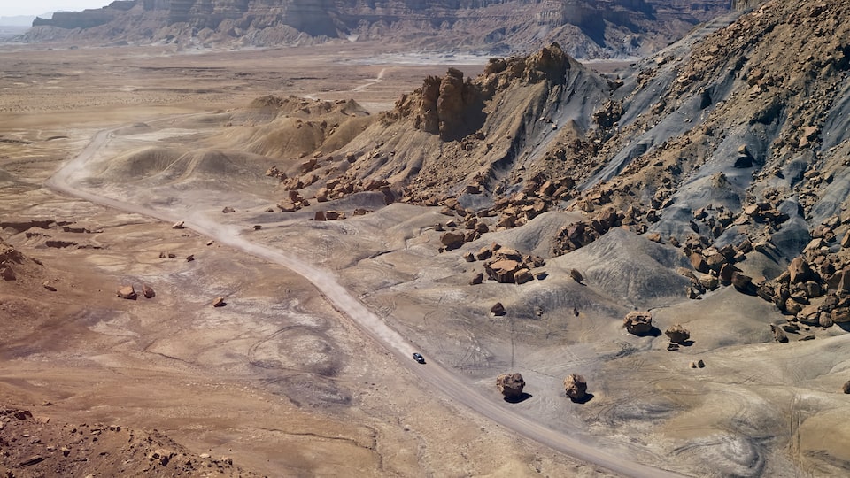 A wide shot of a Chevy Colorado ZR2 Bison far below the camera on a dirt road amid desert brush and mountain faces.