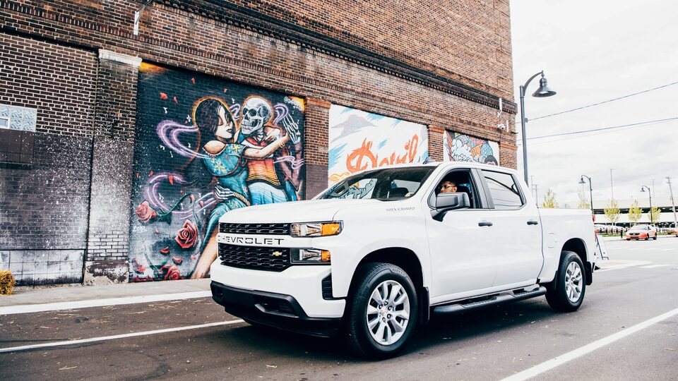 Freddy Diaz in a white Silverado on a Detroit street next to one of Freddy’s colorful murals on the side of a brick building.