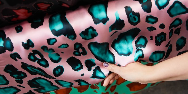A hand pulls some colorful pink and blue fabric down from a bolt of fabric.