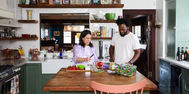 Beth Morgan and a man stand together at a table in a kitchen chopping food.