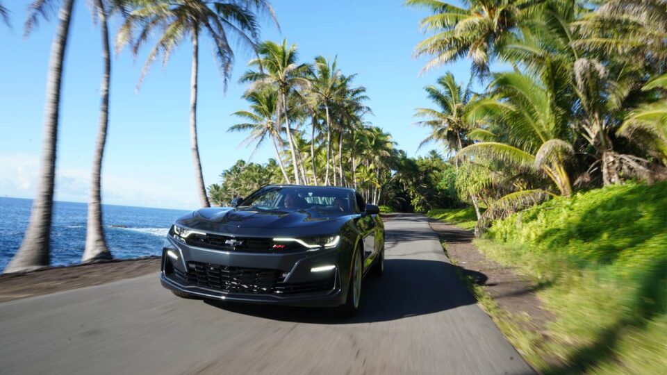 A 2020 Camaro SS is seen from the front on a flat paved road lined with palm trees next to the ocean.