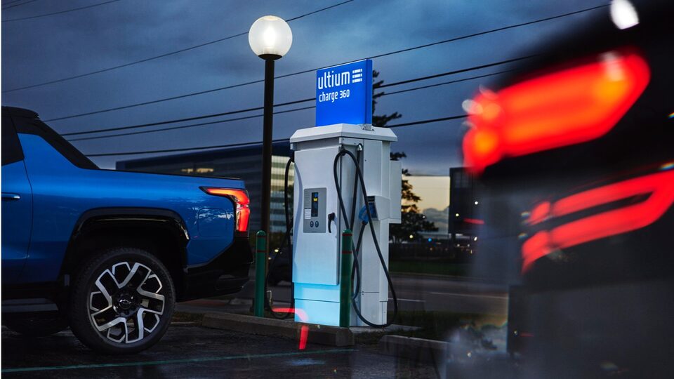 Una Silverado EV azul circulando en reversa hacia un espacio de estacionamiento al lado de un cargador de EV con un cartel en el que se lee Ultium Charge 360