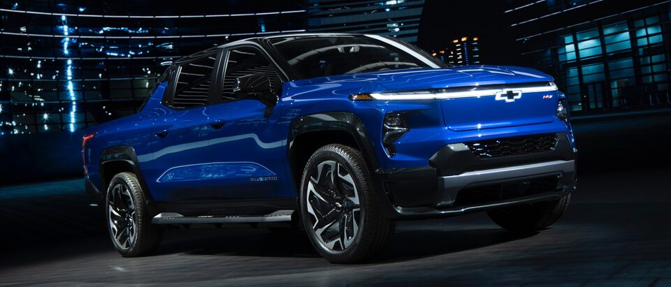 Un Silverado EV azul de noche en una calle de ciudad con las luces de los edificios altos brillando al fondo.