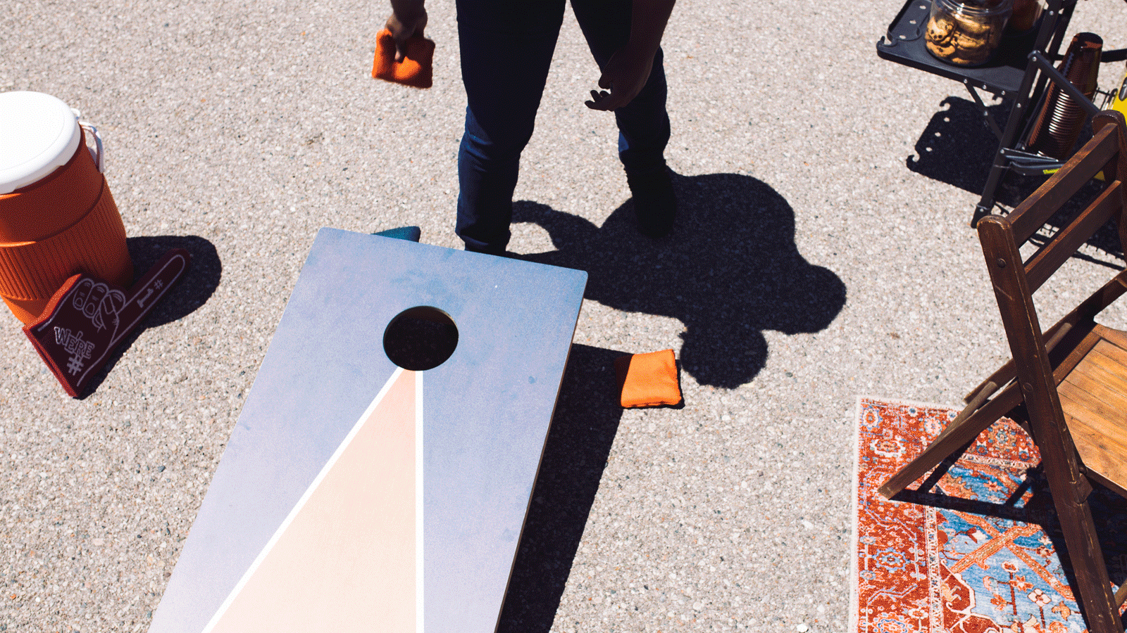 An overhead view of a person about to toss a beanbag while playing a game in a stadium parking lot.
