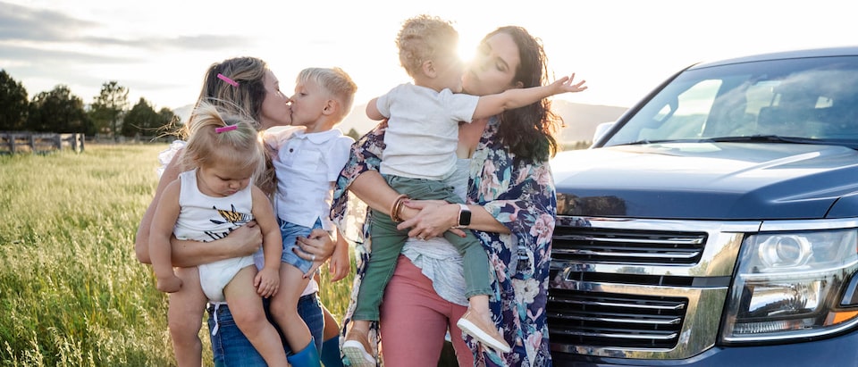 Brittany y Courtney McLachlan con sus hijos en brazos en un campo frente a la Chevrolet Tahoe de Brittany.