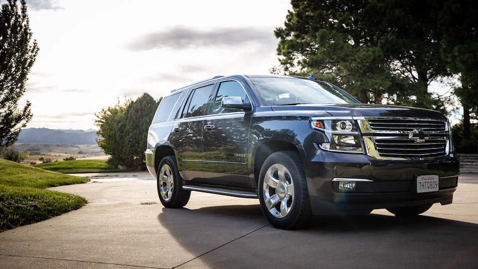 A Chevrolet Tahoe is parked in a driveway with a few trees and other greenery in the background.