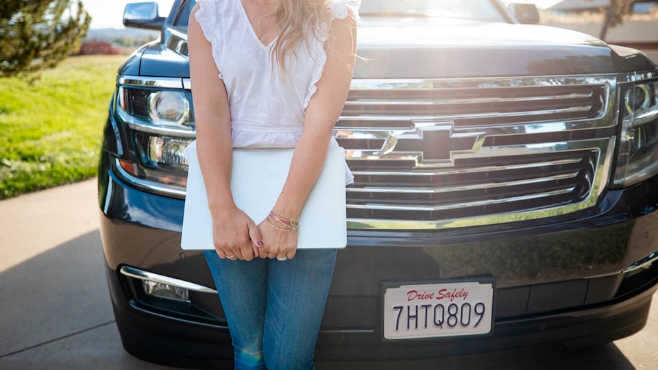 Brittany McLachlan holds a laptop and leans against the front of her Chevrolet Tahoe.