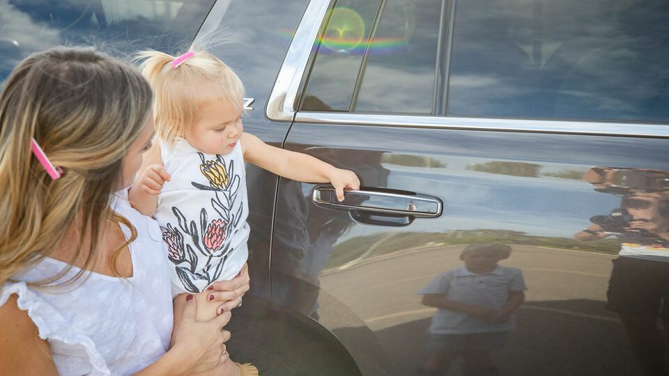 Brittany McLachlan carries her daughter, who holds on to the door handle of Brittany’s Chevrolet Tahoe.