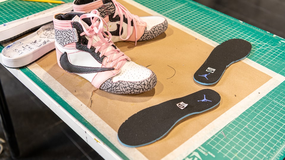 Un par de tenis terminados con un diseño único de rosa y gris con un par de platillas sobre una tabla de cortar tela verde.