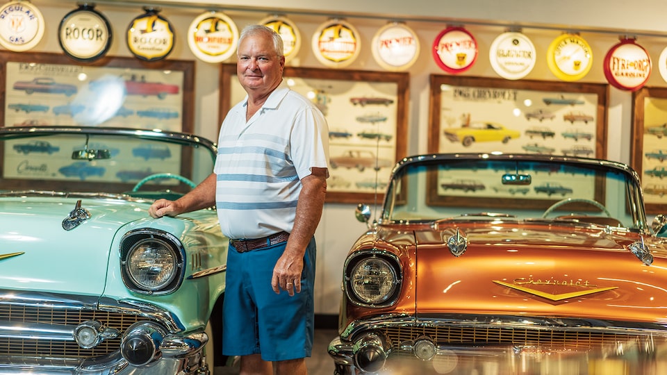 Dennis Albaugh de pie frente a dos convertibles Chevrolet de los años 1950, con la mano sobre uno de ellos.