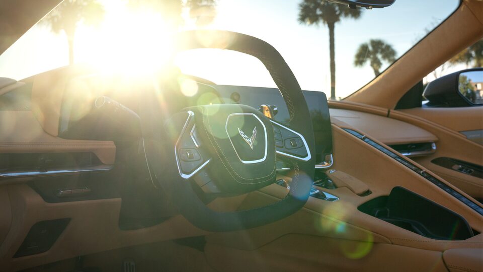 El interior forrado en piel Napa y volante deportivo de un Corvette Convertible 2020; a través del parabrisas se ven unas palmeras y el brillo del sol.