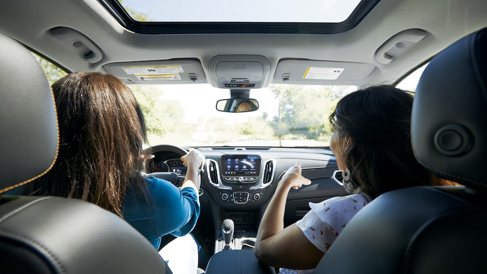 Toma trasera de dos mujeres sentadas en una Chevrolet Equinox, una al volante y la otra señalando a algo en el exterior.