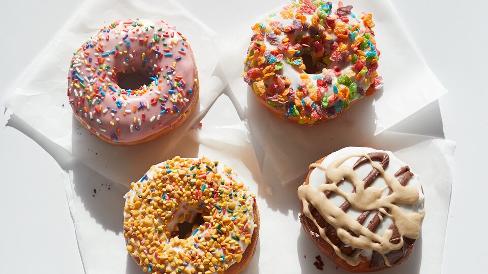 Cuatro donas coloridas con diferentes coberturas y glaseados sobre servilletas, apoyadas en una mesa.