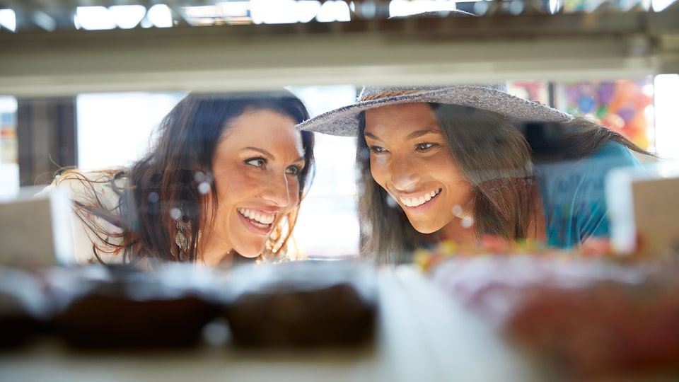 Primer plano de dos mujeres mirando un exhibidor con donas.