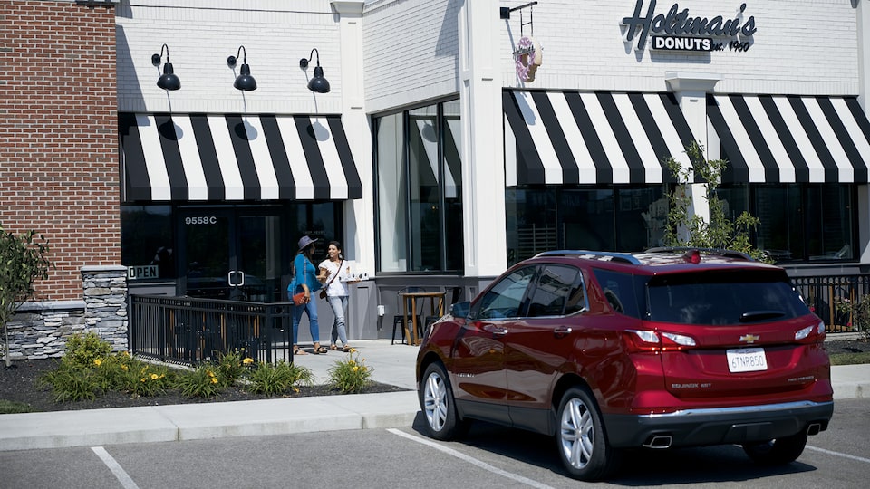 Una Chevrolet Equinox roja estacionada fuera de la tienda Holtman's Donuts, un edificio de ladrillo blanco con un toldo rayado negro y blanco.