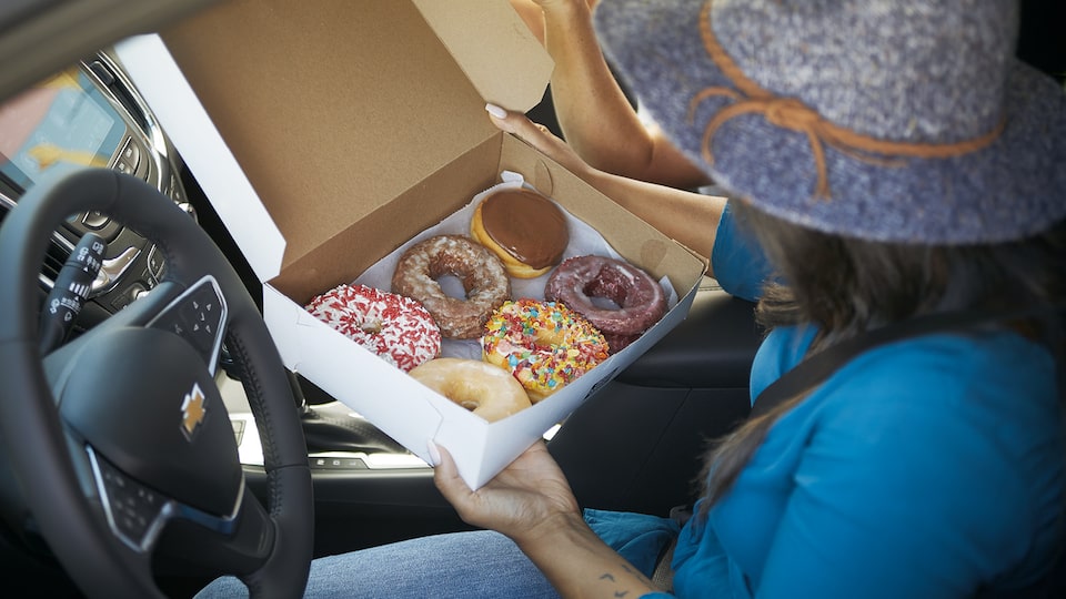 Una mujer sentada en el asiento del conductor de la Chevrolet Equinox, sosteniendo un contenedor de seis donas y mirándolo.