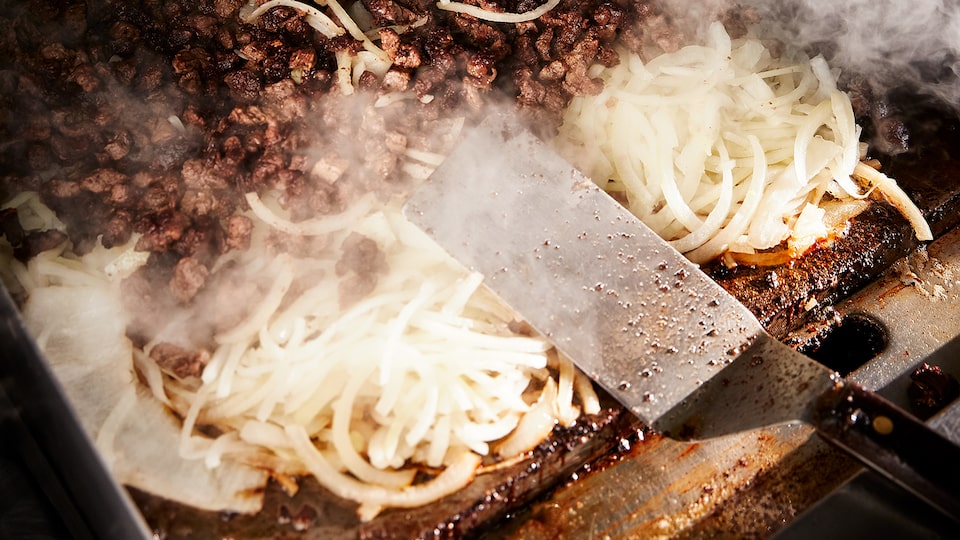 Meat and onions and rising steam on a flat-top grill.