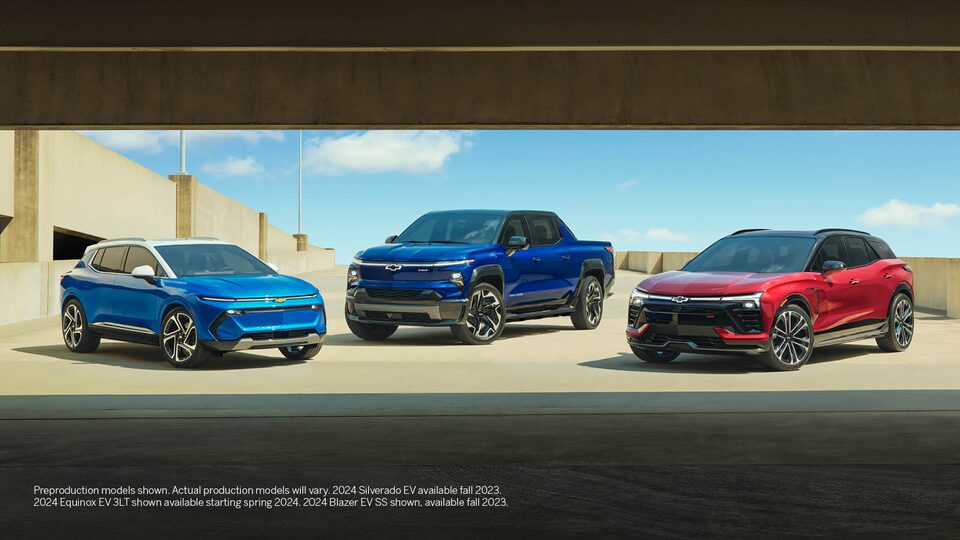Una Equinox EV azul, una Silverado EV azul y una Blazer EV roja estacionadas juntas en el nivel superior abierto de un estacionamiento.