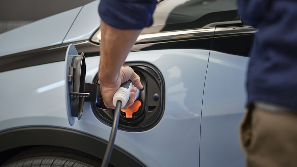 A close-up of a person plugging  a charging cable into the open  charging port on a Bolt EV.