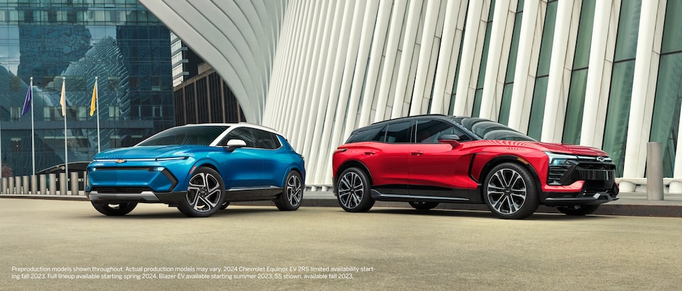 A blue Equinox EV and a red Blazer EV sit side by side next to a contemporary building.
