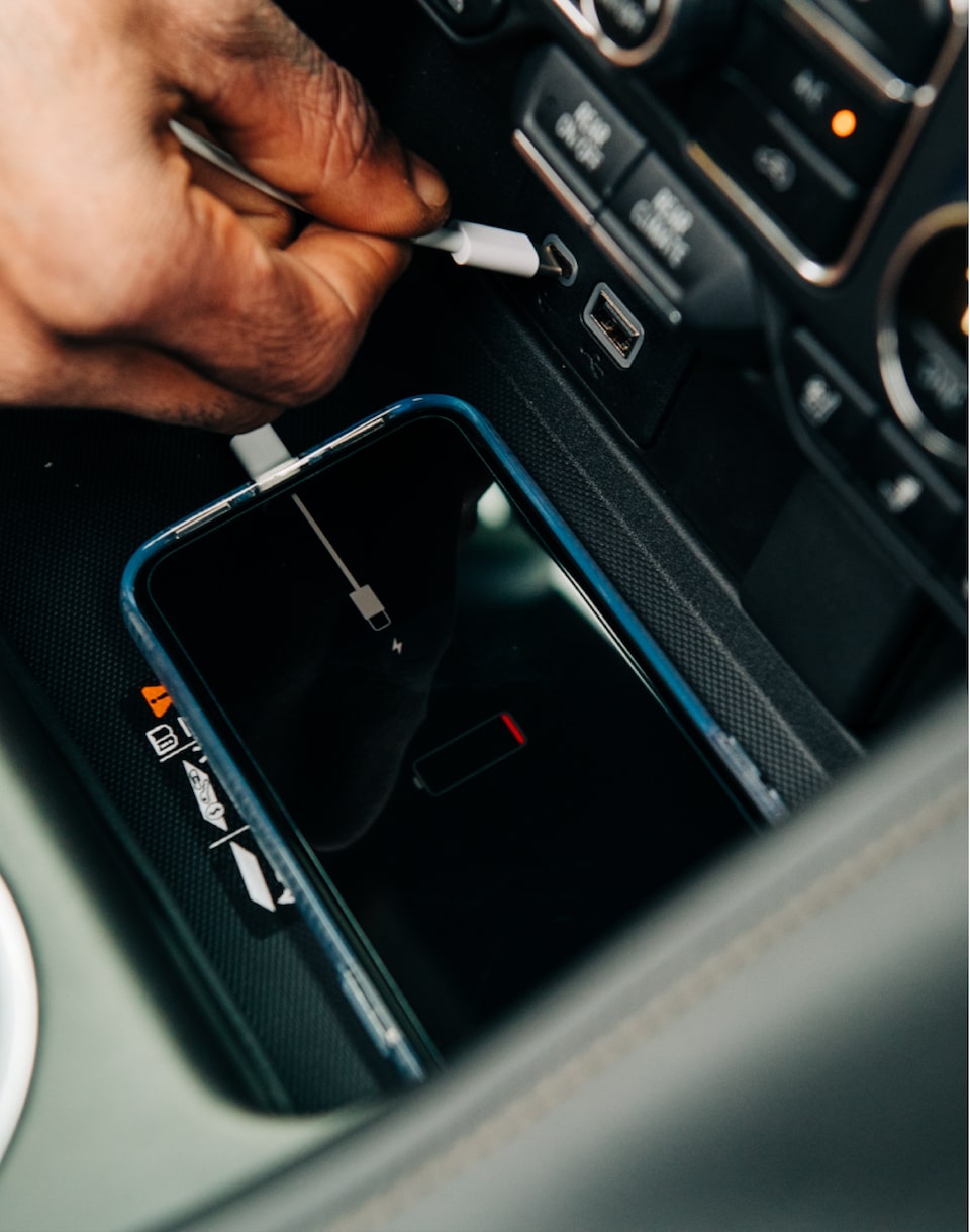 The front of the center console in a 2021 Tahoe, with a person’s hand plugging a smartphone cable into the USB port.