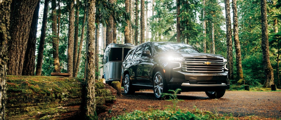 A black 2021 Tahoe pulls an Airstream Basecamp X trailer through a wooded area.