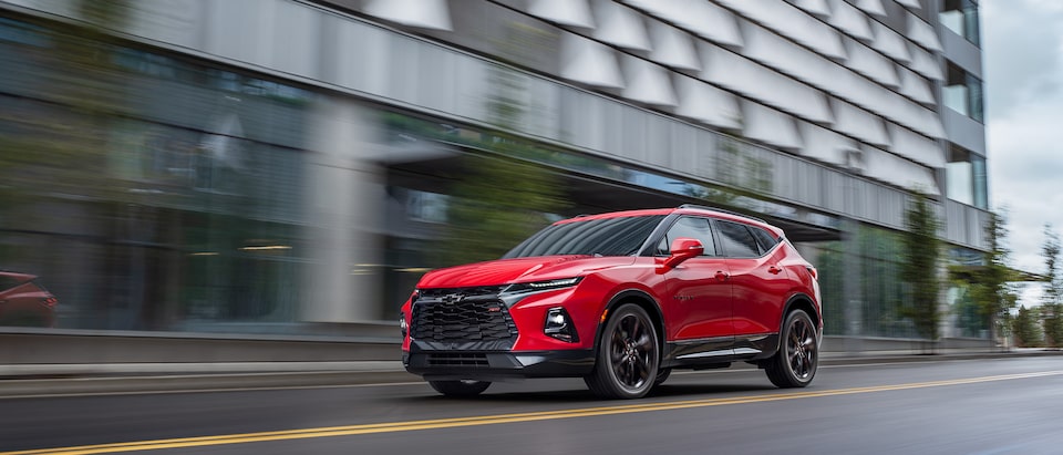 A red Chevy Blazer RS drives past a building, seen from the front driver’s side corner.