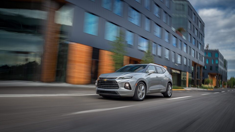 A silver Chevy Blazer Premier drives past a building, seen from the front driver’s side corner.
