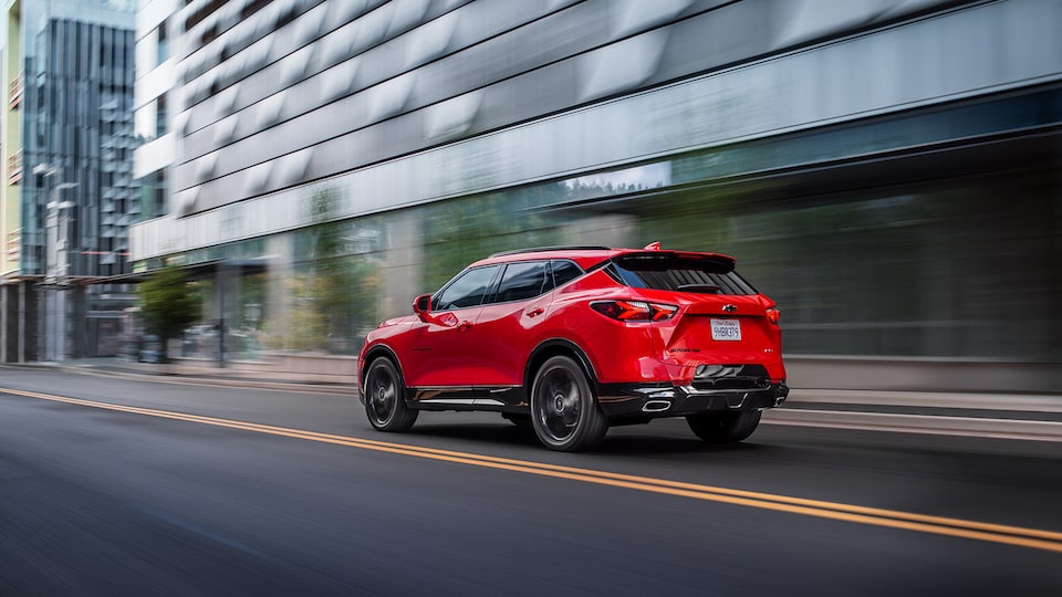 A red Chevy Blazer RS drives past a building, seen from the rear driver’s side corner.