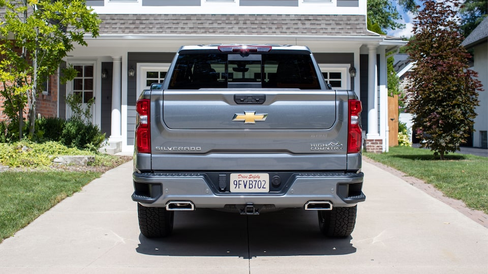 A gray Silverado High Country parked in a driveway, seen from behind with the Multi-Flex Tailgate raised completely.