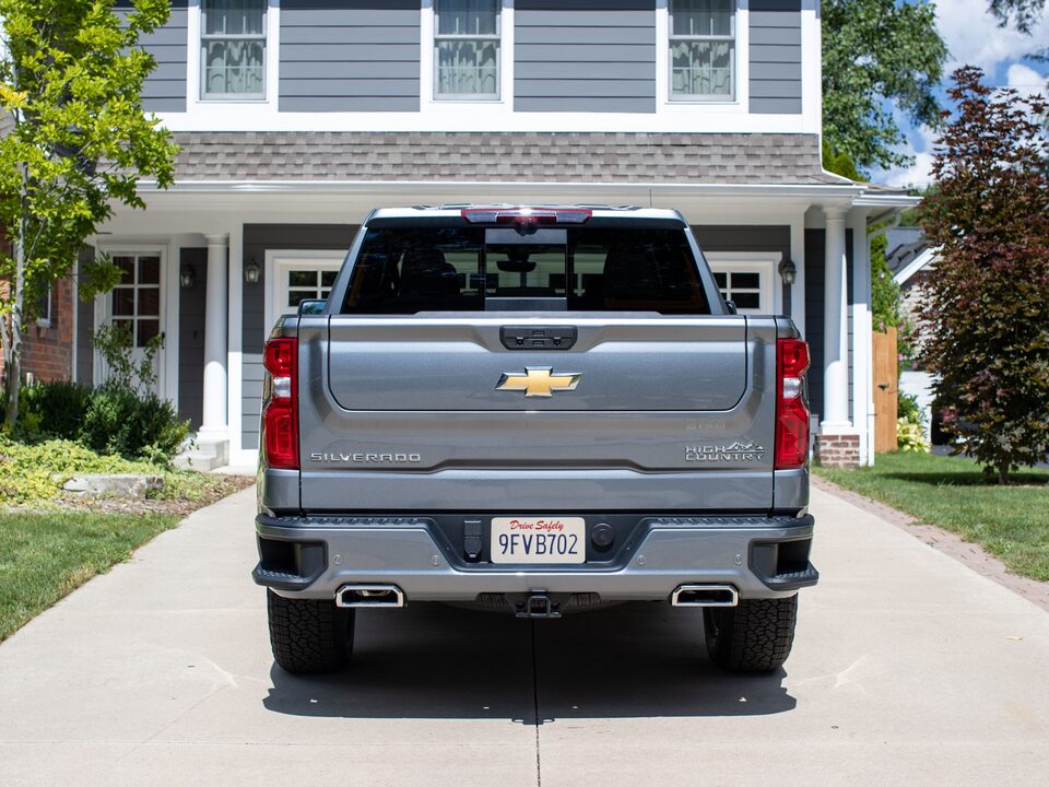 A gray Silverado High Country parked in a driveway, seen from behind with the Multi-Flex Tailgate raised completely.