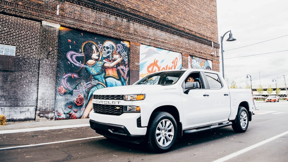 Freddy Diaz in a white Silverado on a Detroit street next to one of Freddy’s colorful murals on the side of a brick building.